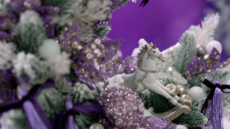 Rocking horse ornament among glittery purple balls, ribbons, and flocked branches creating a festive holiday decorationの写真素材