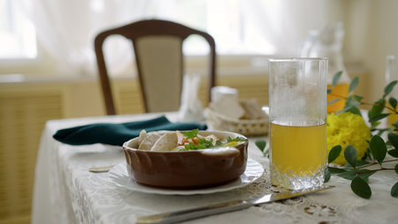 Elegant dining table decorated with fresh greens and yellow flowers, serving a bowl of stew and a glass of juiceの写真素材