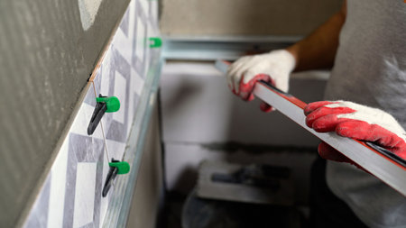 Worker wearing gloves aligning geometric patterned wall tiles with a spirit level tool for home improvement and constructionの写真素材