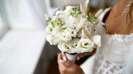 Bride holding a fresh white floral wedding bouquet with delicate lace details, celebrating love and...