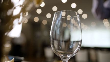 Empty wine glass in an elegant setting. The background features warm, circular bokeh lights creating...