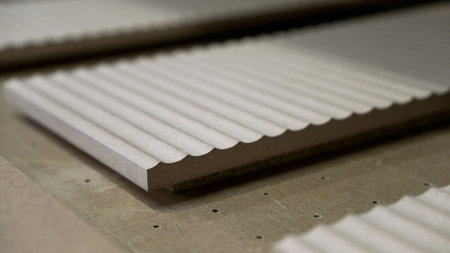 Close-up of milled MDF panel with a wavy, fluted texture. Soft lighting highlights the abstract...