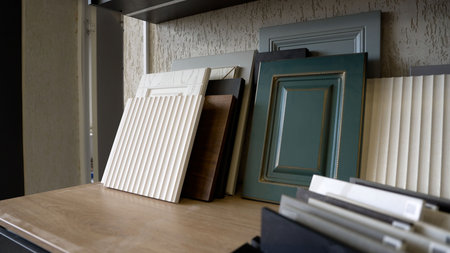 A collection of cabinet door samples for interior design. Various styles, from classic green to modern fluted white, are displayed on a wooden shelf.の写真素材