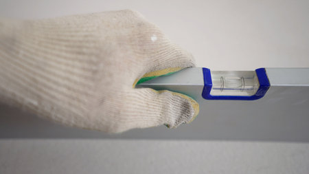 Close-up of a construction worker's hand in a white glove holding a spirit level. The bubble is...