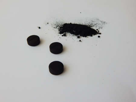 activated charcoal in tablets and in bulk on a white backgroundの写真素材