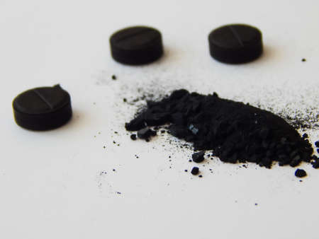 activated charcoal in tablets and in bulk on a white backgroundの写真素材