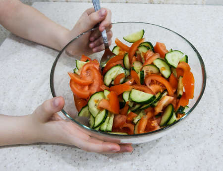 a girl mixes a spoonful of tomato and cucumber salad in a glass thicketの写真素材