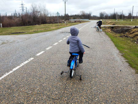 brother and sister ride bicycles on the road in rainy weatherの写真素材