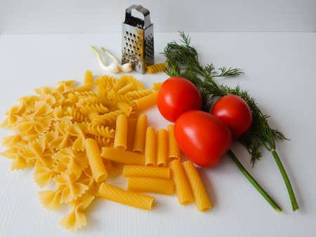 red tomatoes lie next to pasta of various shapes and green dillの写真素材