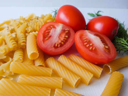 red tomatoes lie next to pasta of various shapes and green dillの写真素材