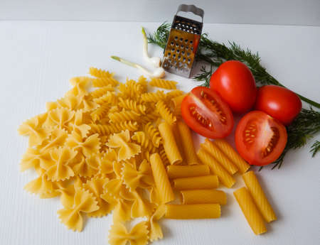 red tomatoes lie next to pasta of various shapes and green dillの写真素材