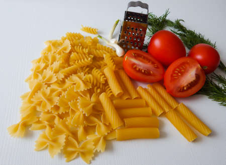 red tomatoes lie next to pasta of various shapes and green dillの写真素材