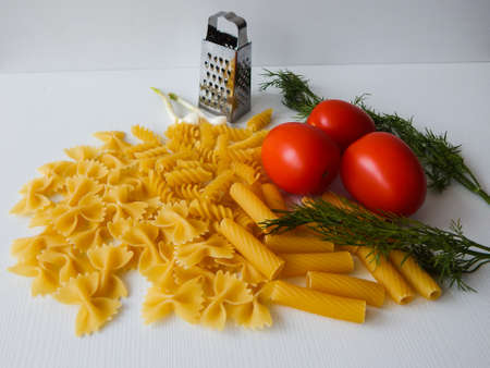 red tomatoes lie next to pasta of various shapes and green dillの写真素材