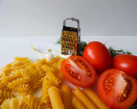red tomatoes lie next to pasta of various shapes and green dillの写真素材