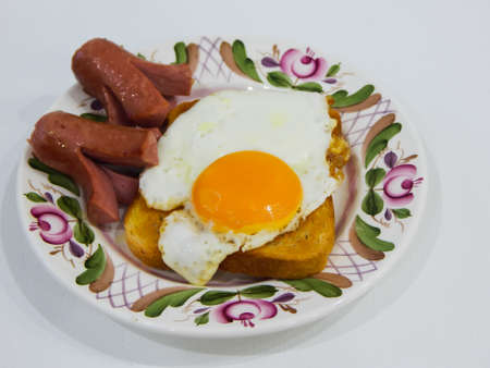 a fried chicken egg lies on a piece of bread and sausages are next to itの写真素材