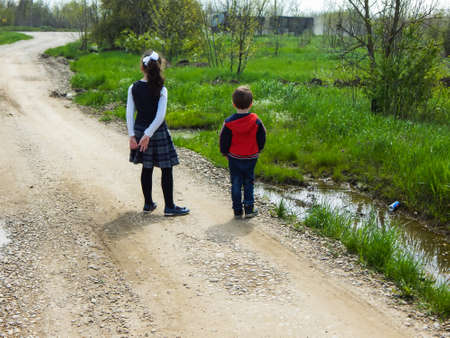 A boy and a girl walk along a dirt road in the spring.