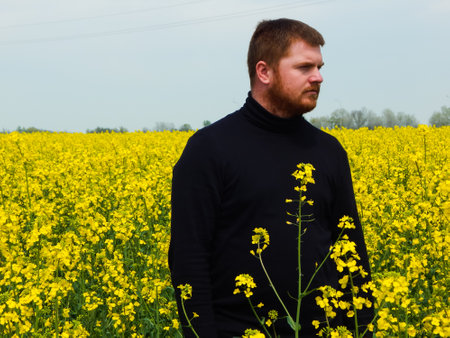 a man stands in a blooming yellow rapeseed fieldの写真素材