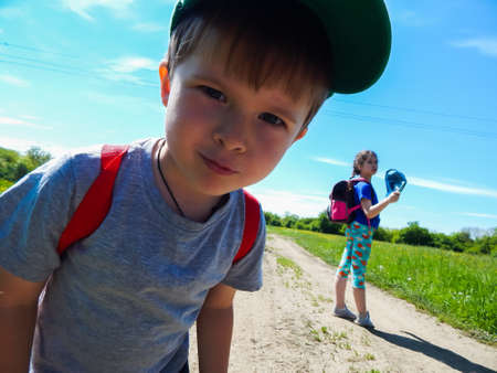 Little boy with backpack and girl on a country road in the summerの写真素材