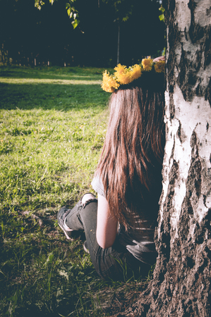 Yellow wreath of dandelions on the girls head with long hair near the tree in the parkの写真素材