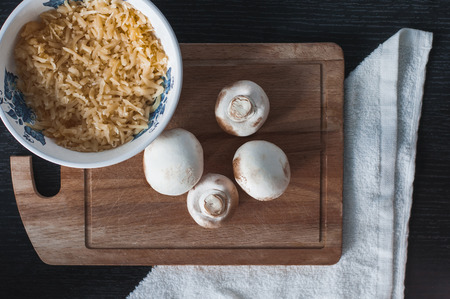 White mushrooms on the wooden board with grated cheese in the plate. Champignon on the desk before cookingの写真素材