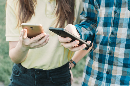 Teenagers watching at their smartphones. Social sharing. Man and female send messagesの写真素材