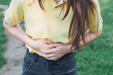 Woman has a pain in the stomach. Teenager has a stomachache outdoors. Holding a hand on the stomachの写真素材