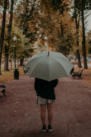 Young woman with blue umbrella in the alley in the autumn parkの写真素材