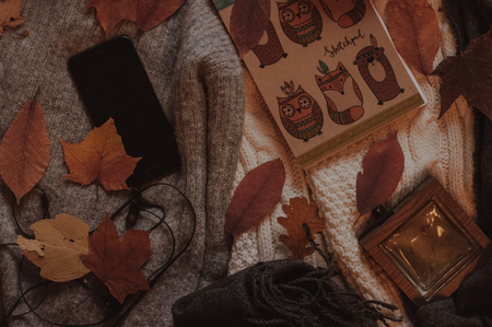 Autumn flatlay. Phone with headphones, cute notebook and scarf top view on the sweaters