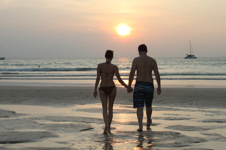 Couple hand in hand in front of sunset on the beach, Thailand, Nai Harn Beachの写真素材