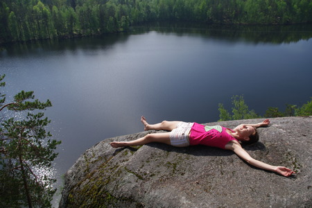 young woman lying and relaxing on the top of a cliff above the lake Yastrebinoye,  Priozersky district, Leningrad region, Russiaの写真素材