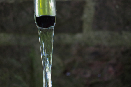 Close up of running water from a tap with brick wall in backgroundの写真素材
