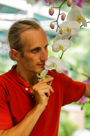 a handsome young man in garden smelling beautiful flowers in a sunny dayの写真素材
