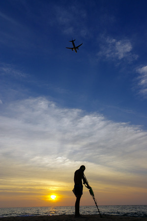 a treasure hunter with Metal detector on sunset on the beach, with a plan in the sky.の写真素材