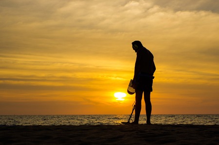 a treasure hunter with Metal detector on sunset on the beachの写真素材