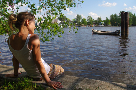 a girl sitting on pier and looking at the river. Woman relaxing by a lake.の写真素材