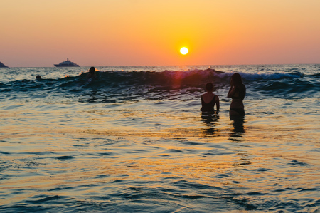 scenic beautiful romantic sunset over sea with people silhouette in standing in water and enjoy the evening orange sun at adaman ocean, Patong Beach Phuket island, Thailandの写真素材
