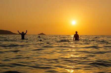 scenic beautiful romantic sunset over sea with people silhouette in standing in water and enjoy the evening orange sun at adaman ocean, Patong Beach Phuket island, Thailandの写真素材