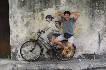PENANG, MALAYSIA - APRIL 18, 2016: a Local tourist poses in-front of Street Mural tittle 'Little Children on a Bicycle' painted by Ernest Zacharevic in Penang on July 6, 2013 in George Townのeditorial素材