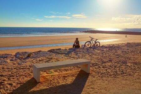 girl with a bicycle listens to music on headphones at the beach