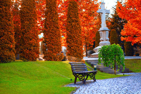 Red trees and green lawn in the park . Summer and autumn scenery . Monument of orthodox crossの写真素材