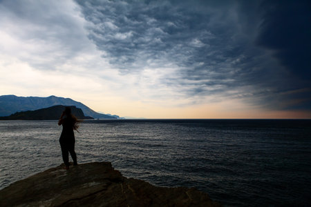 Girl standing on the seaside in the stormy weather and taking a pictures by smartphone . Altocumulus dark clouds over the seaの写真素材