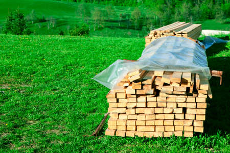 Stack of wood boards on the grass . Stacked wooden planks for rustic house construction . Country home conceptの写真素材