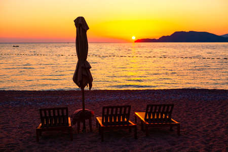 Chaise lounges and umbrella on the beach in the twilight . Fantastic coastal summer vacation . Beach on the island in the evening . Sunset over the seaの写真素材