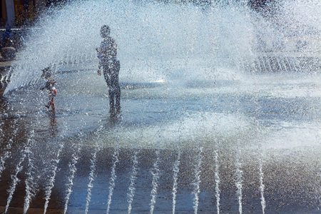 People silhouette in ground fountain . Little girl enjoying the fountain splashingの写真素材