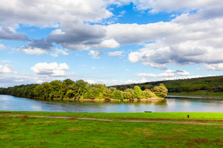 Rustic riverside scenery . Low clouds over the green island . Pasture on the green shore