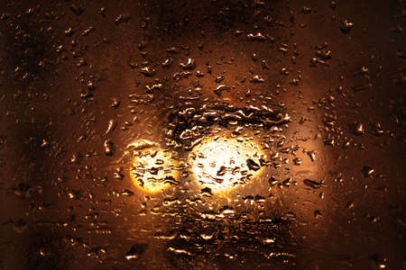 Drops on the glass with glare . Rainy night weather . Wet surface with dark background