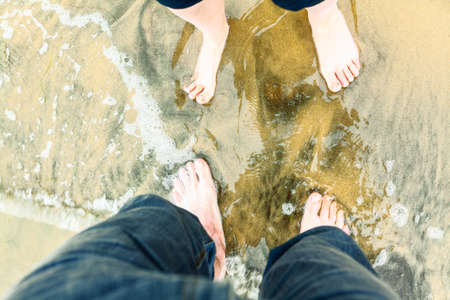 Two pairs of feet in the sand of the sea . Four legs on the sea water . Romantic Rendezvous on the...