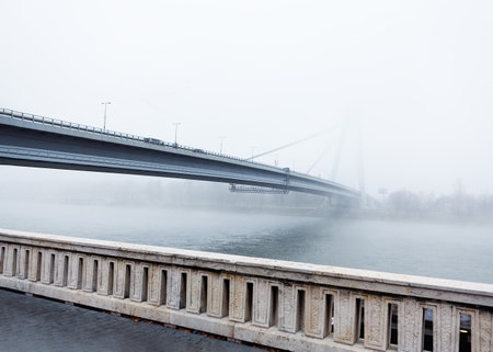 Balustrade and bridge over Danube . Fog over the river in the morning . Riverside sidewalk with...