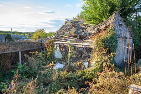 Old ruined hut in village with overgrown yard . Abandoned rustic house