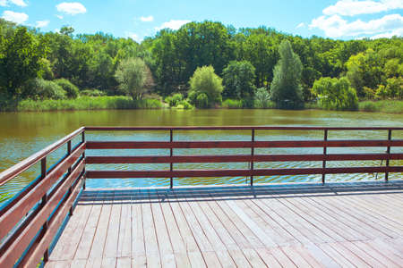 Observation deck with wooden balustrade at the lake . Pond on a summer day